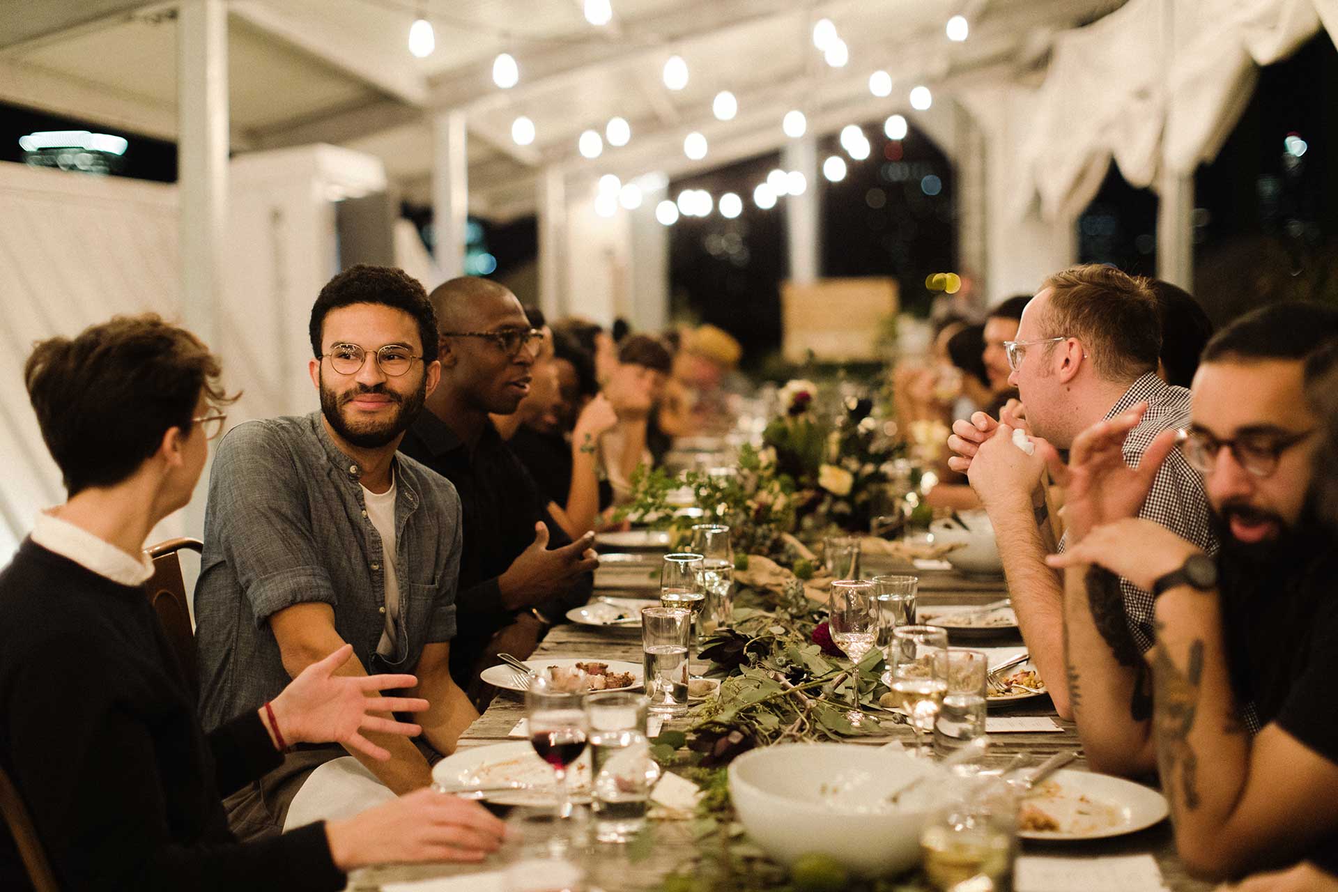 Two dozen people sit in two rows, facing each other over a dinner table.