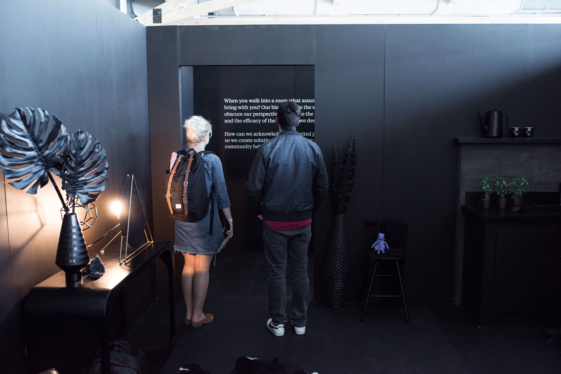 Two people stand in a black and gray living room reading display text.