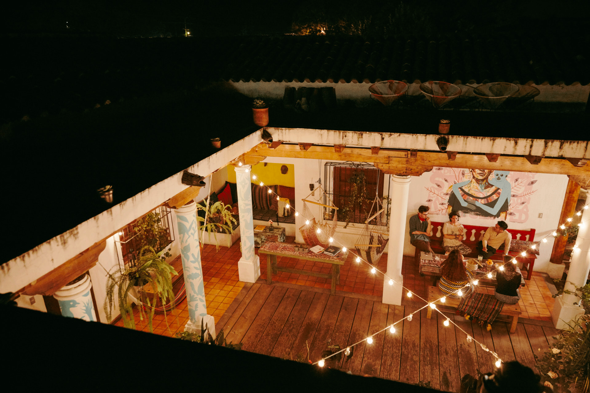 An overhead shot of a small group of people conversing in a courtyard strung with twinkle lights.