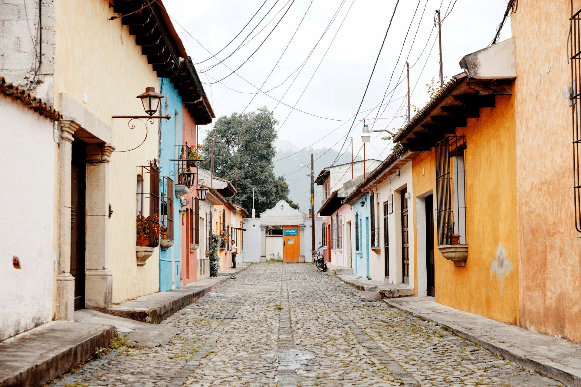 A cobblestone street with brighly colored houses on either side and telephone wires hanging overhead.