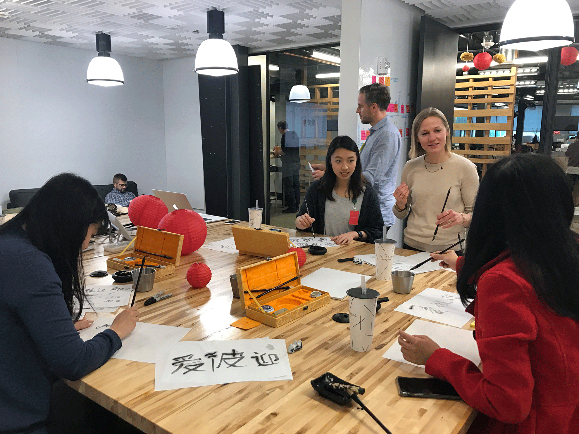 A group of people sit around a table making Chinese calligraphy.